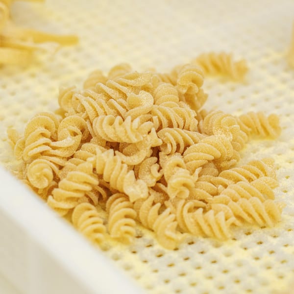 Close-up of freshly made, uncooked fusilli pasta dusted with flour on a drying rack.