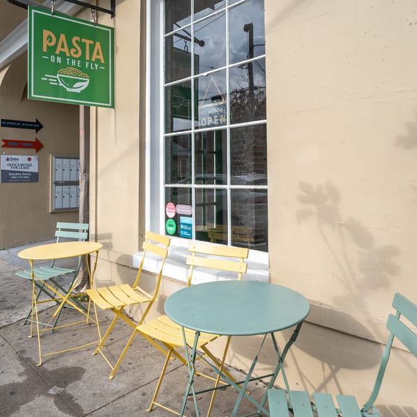 Pasta On The Fly restaurant exterior with green sign, window, and yellow and green outdoor seating.