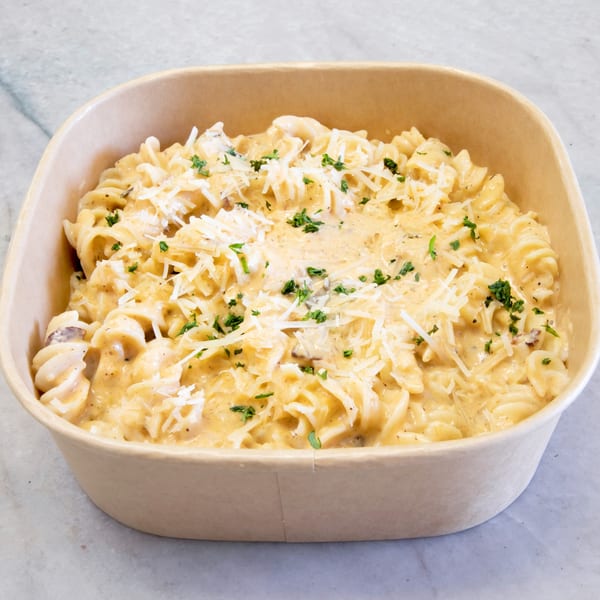 Creamy fusilli pasta with grated cheese and parsley in a brown takeout container.