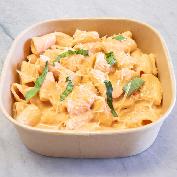 Pasta On The Fly's rigatoni pasta with creamy orange sauce, shredded cheese, and basil in a to-go container.