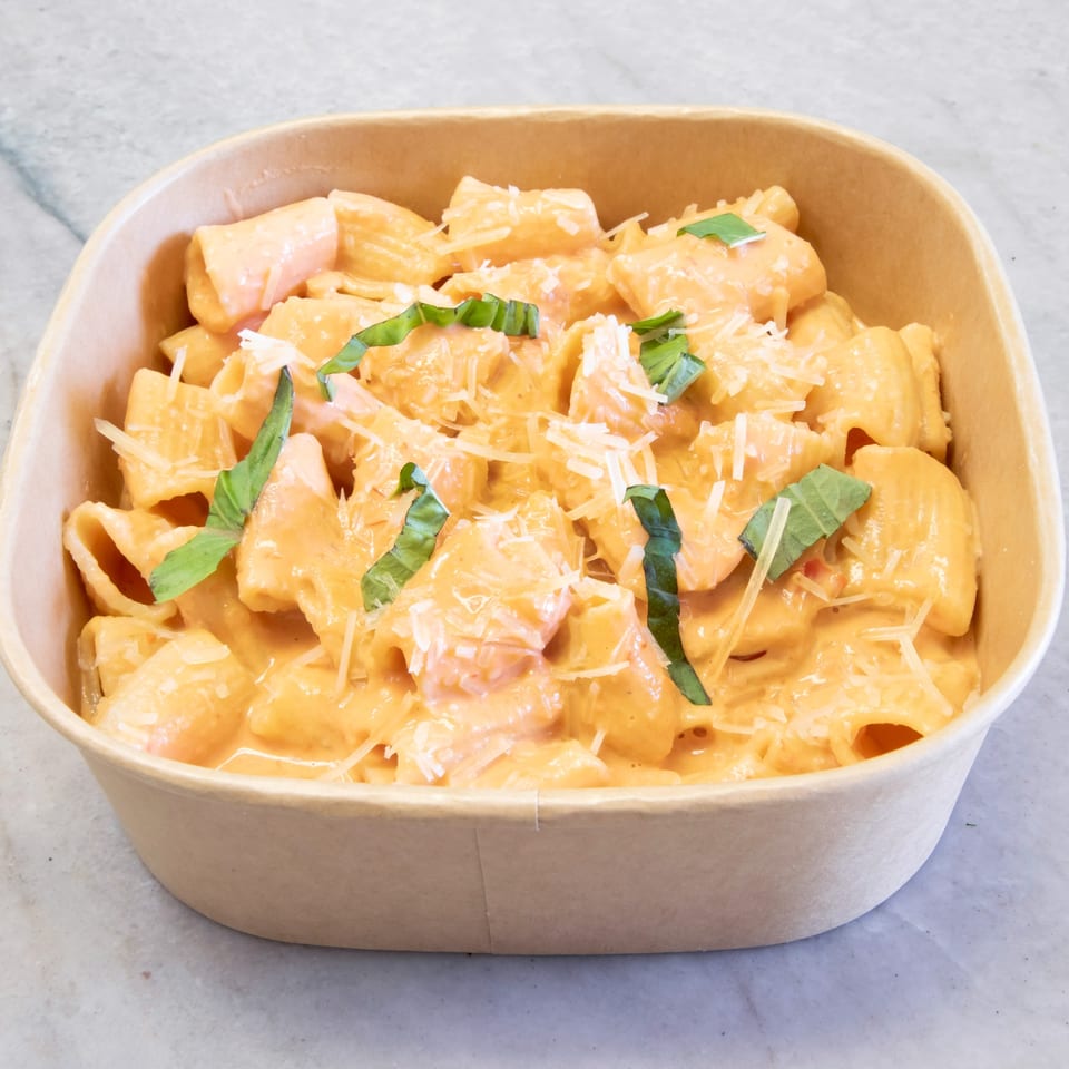 Pasta On The Fly's rigatoni pasta with creamy orange sauce, shredded cheese, and basil in a to-go container.