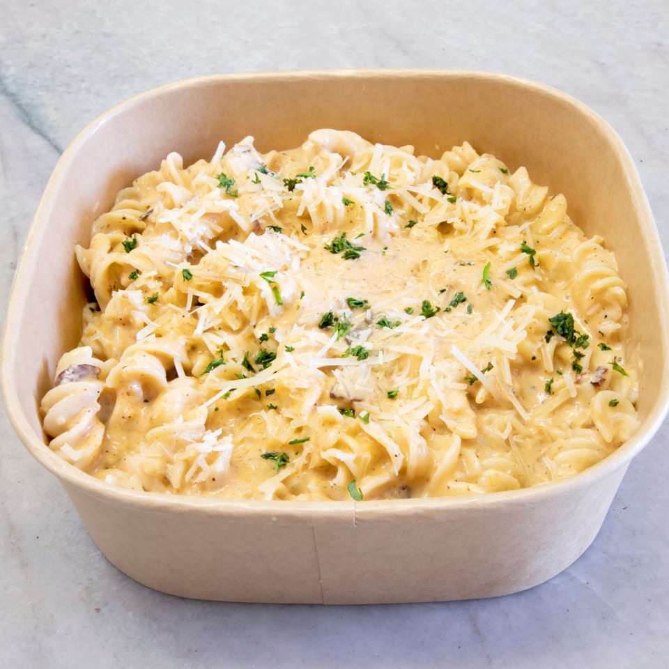 Creamy fusilli pasta with mushrooms, topped with grated cheese and fresh parsley in a brown container.