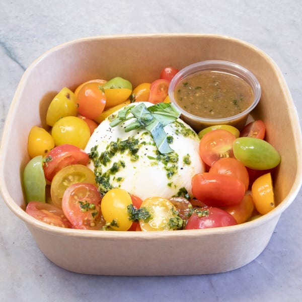 Burrata cheese with pesto and colorful cherry tomatoes in a brown takeout container from Pasta On The Fly.