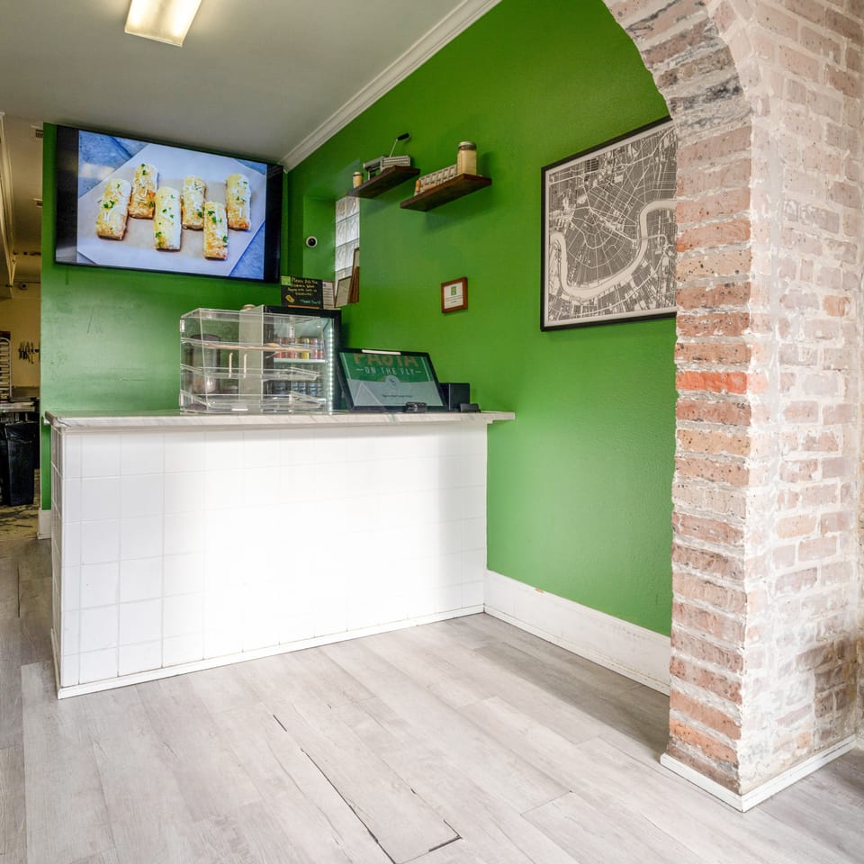 Pasta On The Fly's counter with a menu screen displaying garlic bread, green walls, and a brick archway.