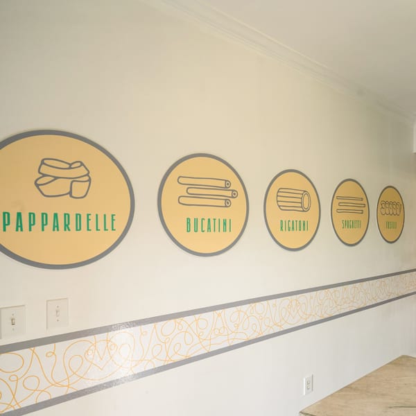 Wall decor at Pasta On The Fly with circular signs depicting different pasta shapes like pappardelle and rigatoni.