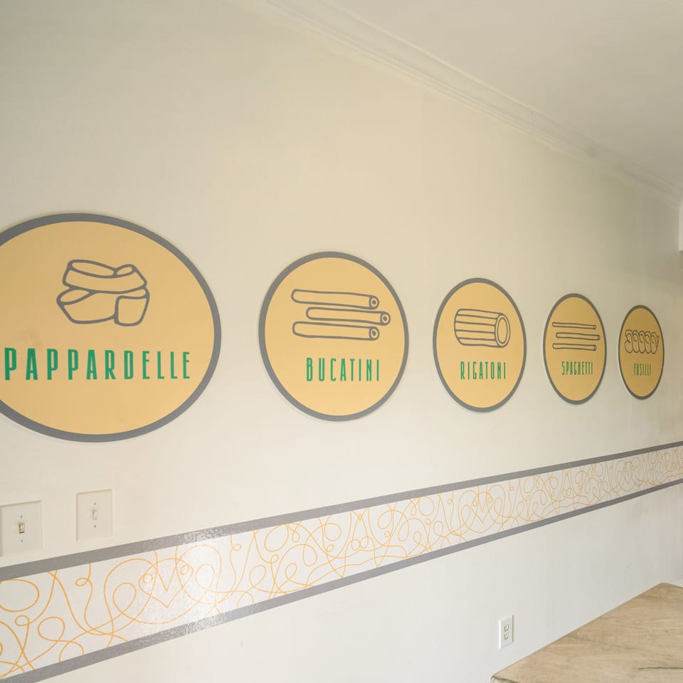 Wall decor at Pasta On The Fly with circular signs depicting different pasta shapes like pappardelle and rigatoni.