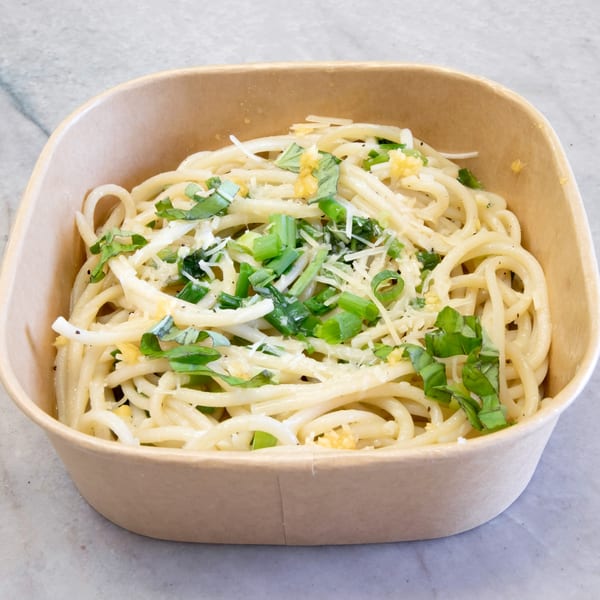 Pasta On The Fly's spaghetti with garlic, basil, and grated cheese in a brown takeout container.