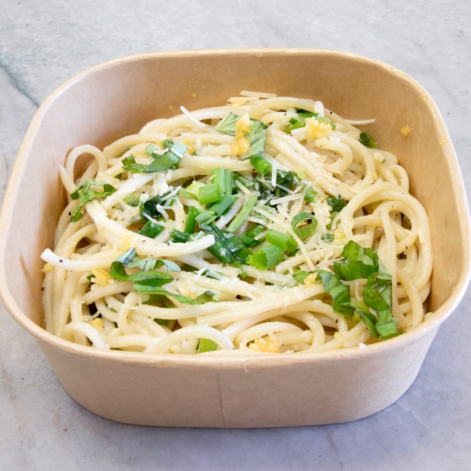 Pasta On The Fly's spaghetti with garlic, basil, and grated cheese in a brown takeout container.