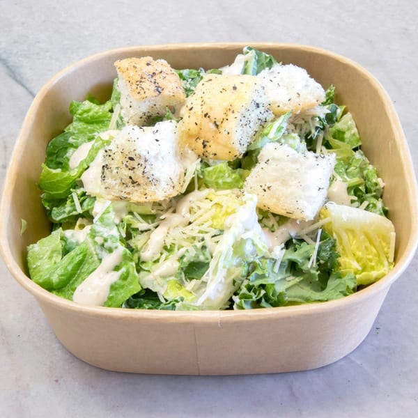 Caesar salad with romaine lettuce, croutons, parmesan cheese, and dressing in a brown takeout container.