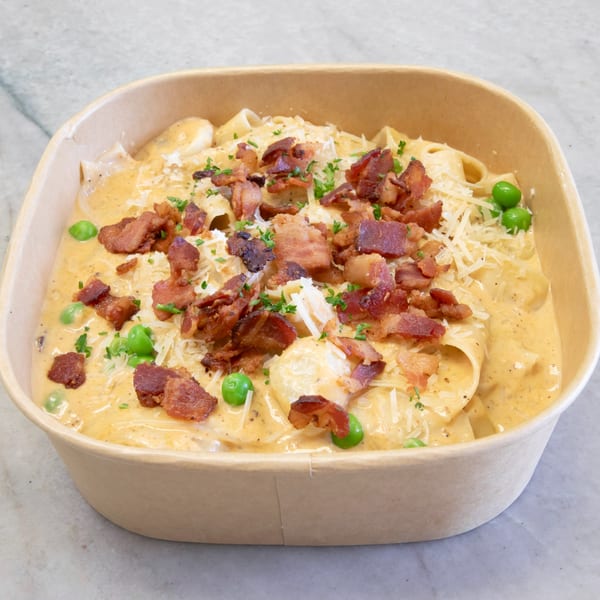 Creamy pasta with bacon, peas, and parmesan cheese in a brown takeout container.